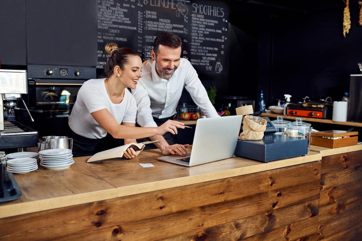 Dois gestores em balcão de restaurante fazendo o planejamento e utilizando um notebook.
