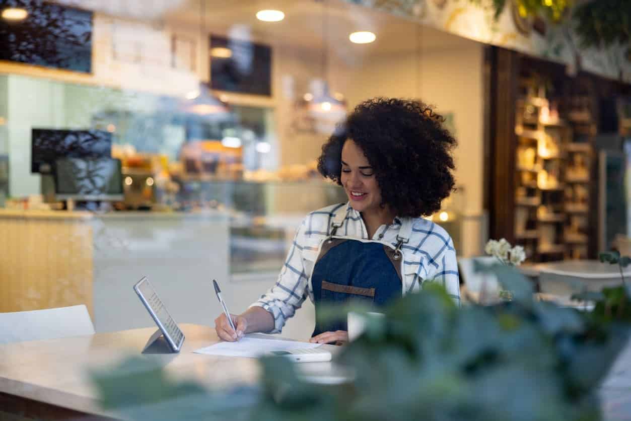 Mulher em restaurante anotando em caderno o planejamento.