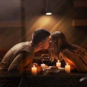Casal jovem feliz se beijando, bebendo vinho tinto tendo jantar romântico.