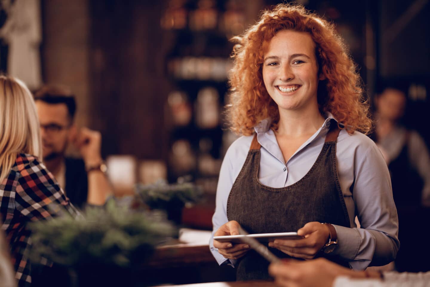 portrait happy redhead waitress holding touchpad while standing pub looking camera