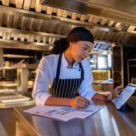 Chef de cozinha moderna usando tablet em cozinha profissional, planejando a gestão.