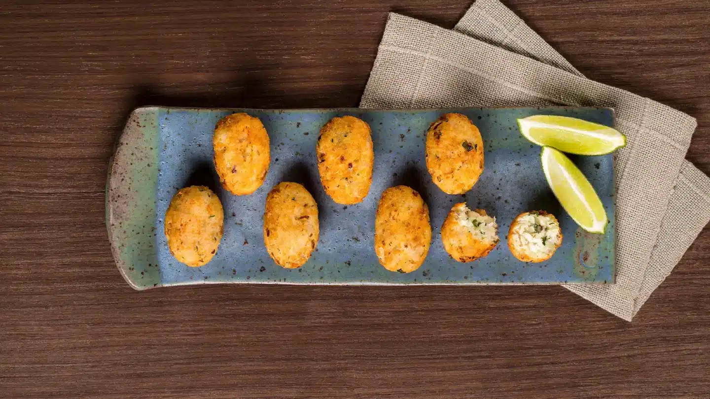 Bolinhos de peixe em uma louça azul com duas fatias de limão ao lado.
